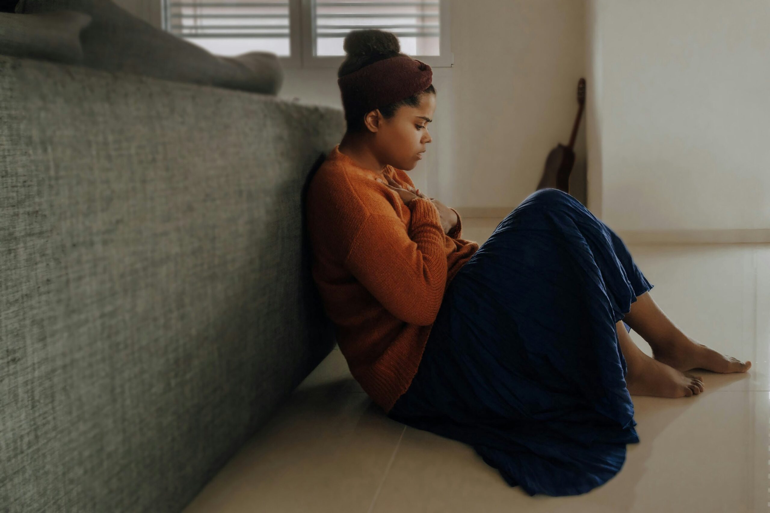 A person sitting on the floor, leaning against a couch, appears contemplative, embodying the theme of managing anxiety levels.
